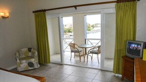 Een hotelkamer met een bed, een televisie, een stoel, een tafel en een balkon met uitzicht.