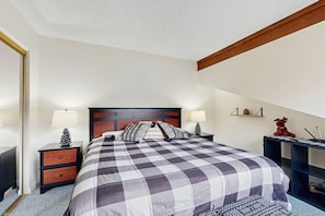 Ein Schlafzimmer mit einem großen Bett, zwei Nachttischen inklusive Lampen, einem Holz-Kopfteil, einem Beistelltisch, einem Schreibtisch mit Computer und einem Regal mit Dekoration.