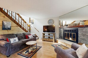 Una sala de estar con una escalera de madera, chimenea, televisor y sofá.