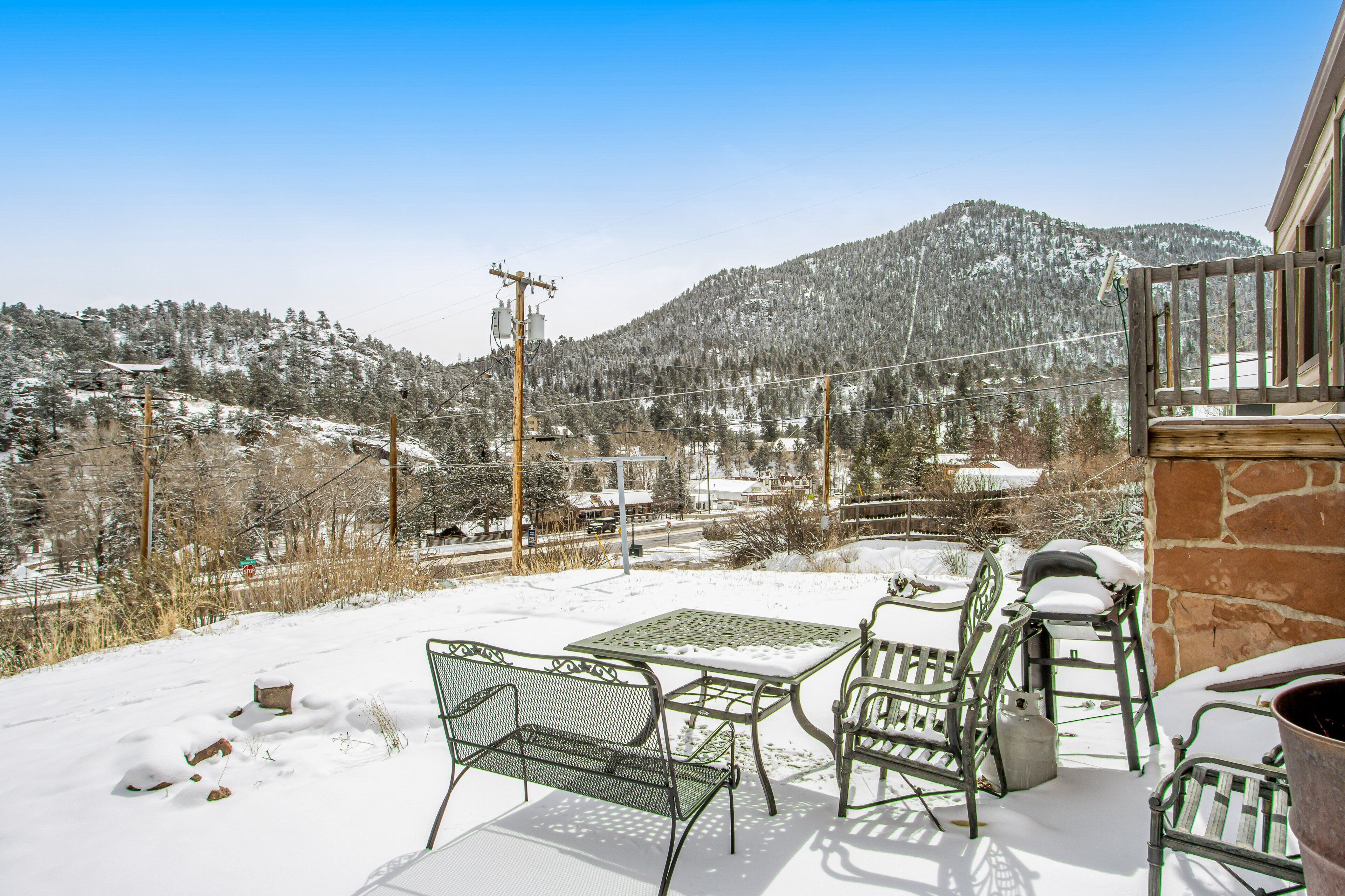 Une terrasse enneigée, agrémentée de mobilier d’extérieur, un mur en pierre et une vue sur une montagne recouverte de neige.