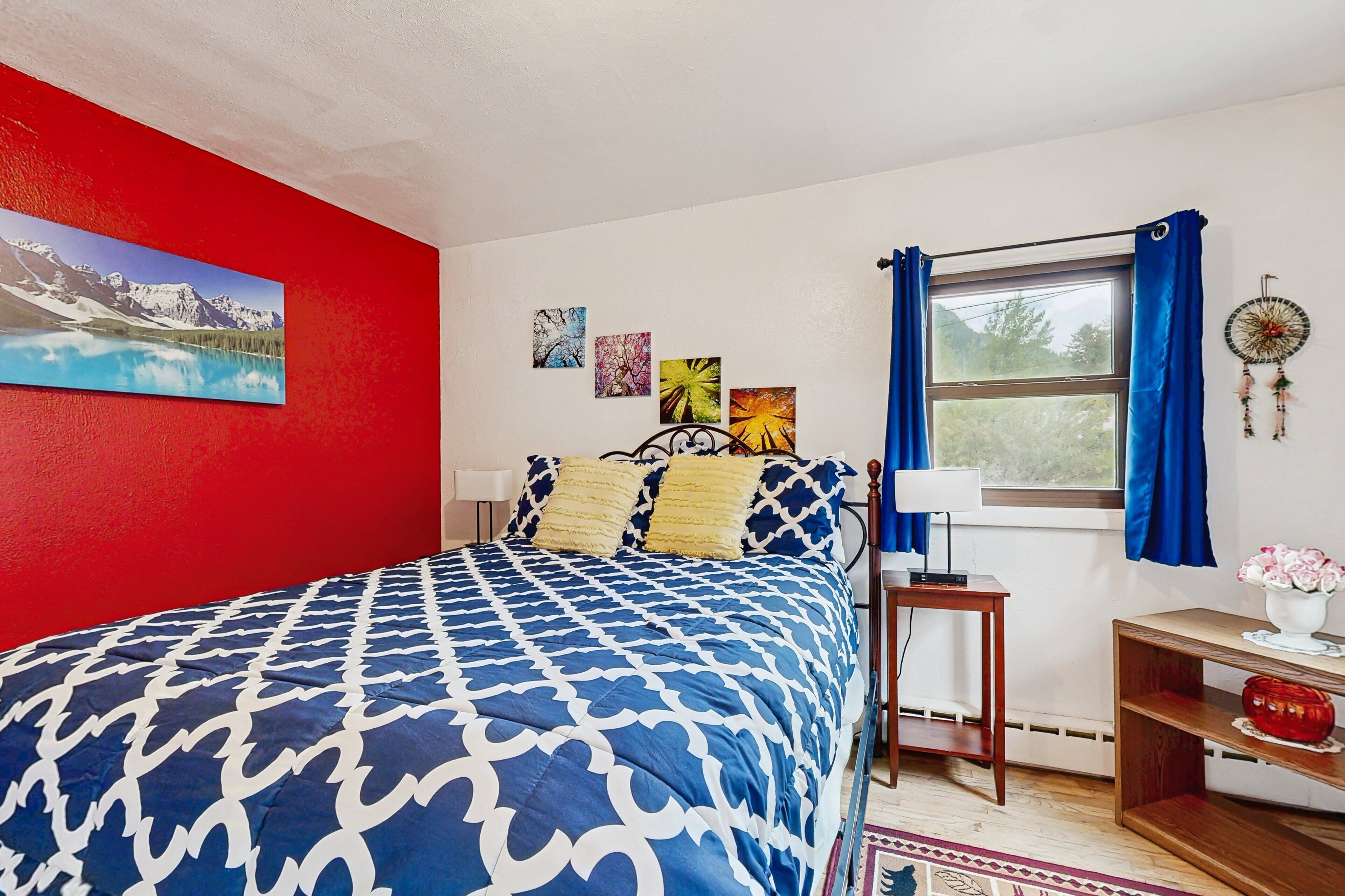 A bedroom with a bed, a desk, a window with curtains, and wall art.