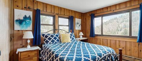 Habitación con paneles de madera, una cama, dos mesitas de noche y dos ventanas.
