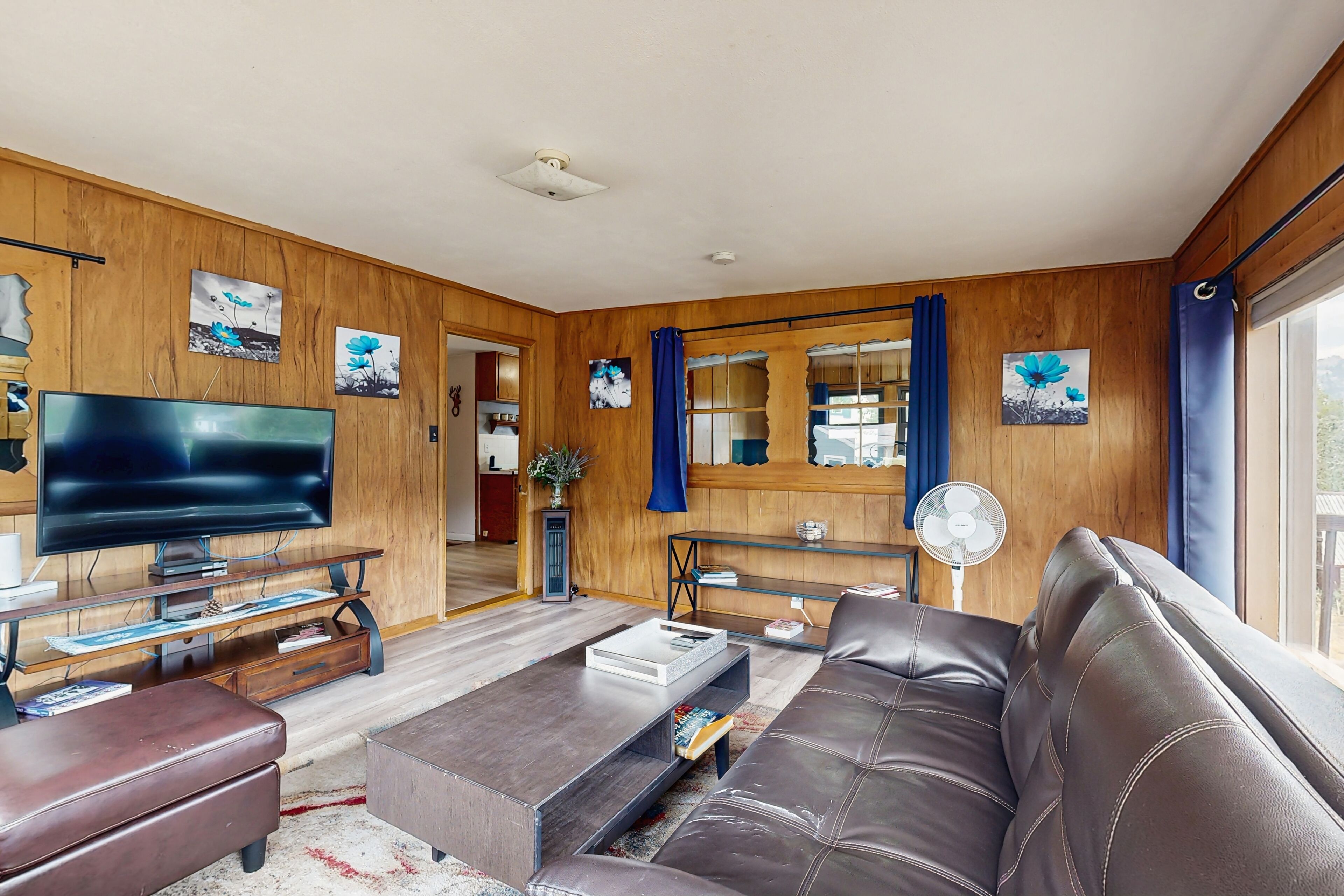 A living room with a leather sofa, a flat-screen TV, wooden walls, and artwork.