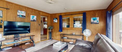 A living room with a leather sofa, a flat-screen TV, wooden walls, and artwork.