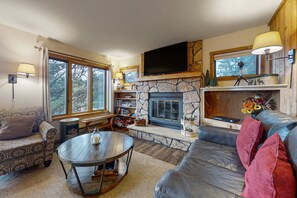 A cozy living room with a stone fireplace, leather sofa, and a television mounted above it. - Inviting Cabin With Stellar Panoramic Rocky Mountain Views (Estes Park)