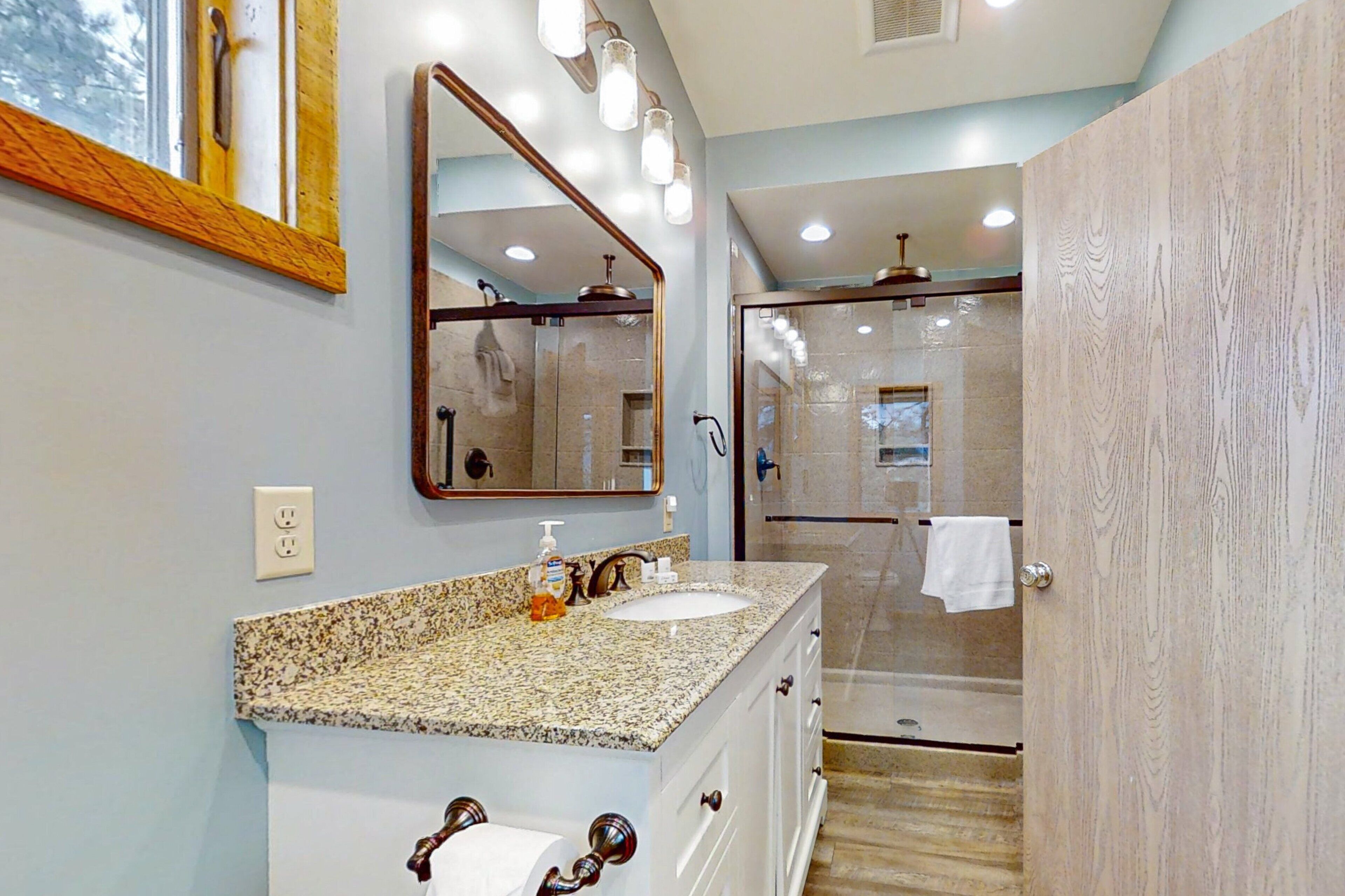 A bathroom with a granite countertop sink, a large mirror, and a walk-in shower.
