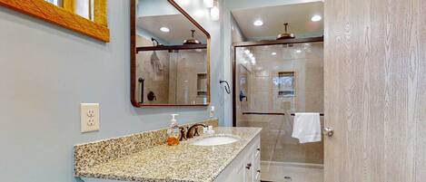 Un baño con lavamanos de encimera de granito, un espejo grande y una ducha a ras de suelo.