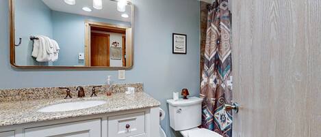 A bathroom with a sink, mirror, toilet, and patterned shower curtain.