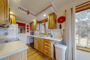 A kitchen with wooden cabinets, a sink, a window, and a trash bin. - Inviting Cabin With Stellar Panoramic Rocky Mountain Views (Estes Park)