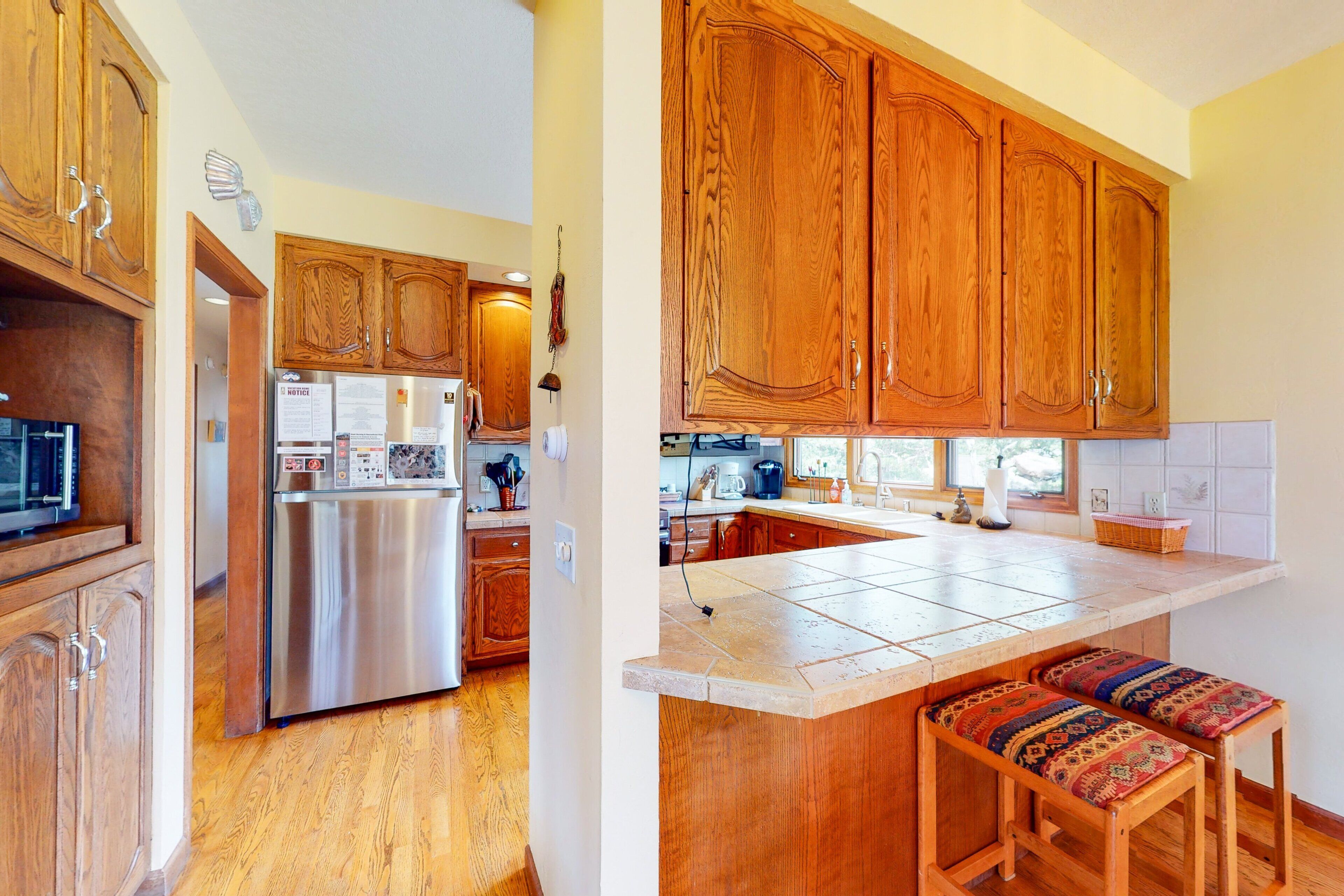 A kitchen with wooden cabinets, a stainless steel refrigerator, and a tiled island with stools.