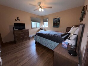 Ein Schlafzimmer mit Bett, Schminktisch, Fernseher, Deckenventilator, Fenstern und Kunstwerken.