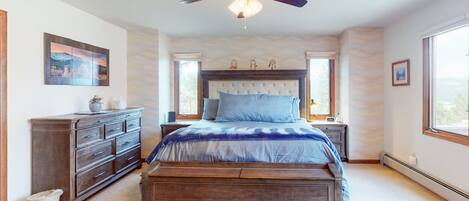 A bedroom with a bed, dresser, nightstands, ceiling fan, and large windows.