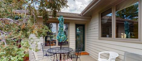 A covered patio with a round table and chairs, a bench, and a door with a glass panel.