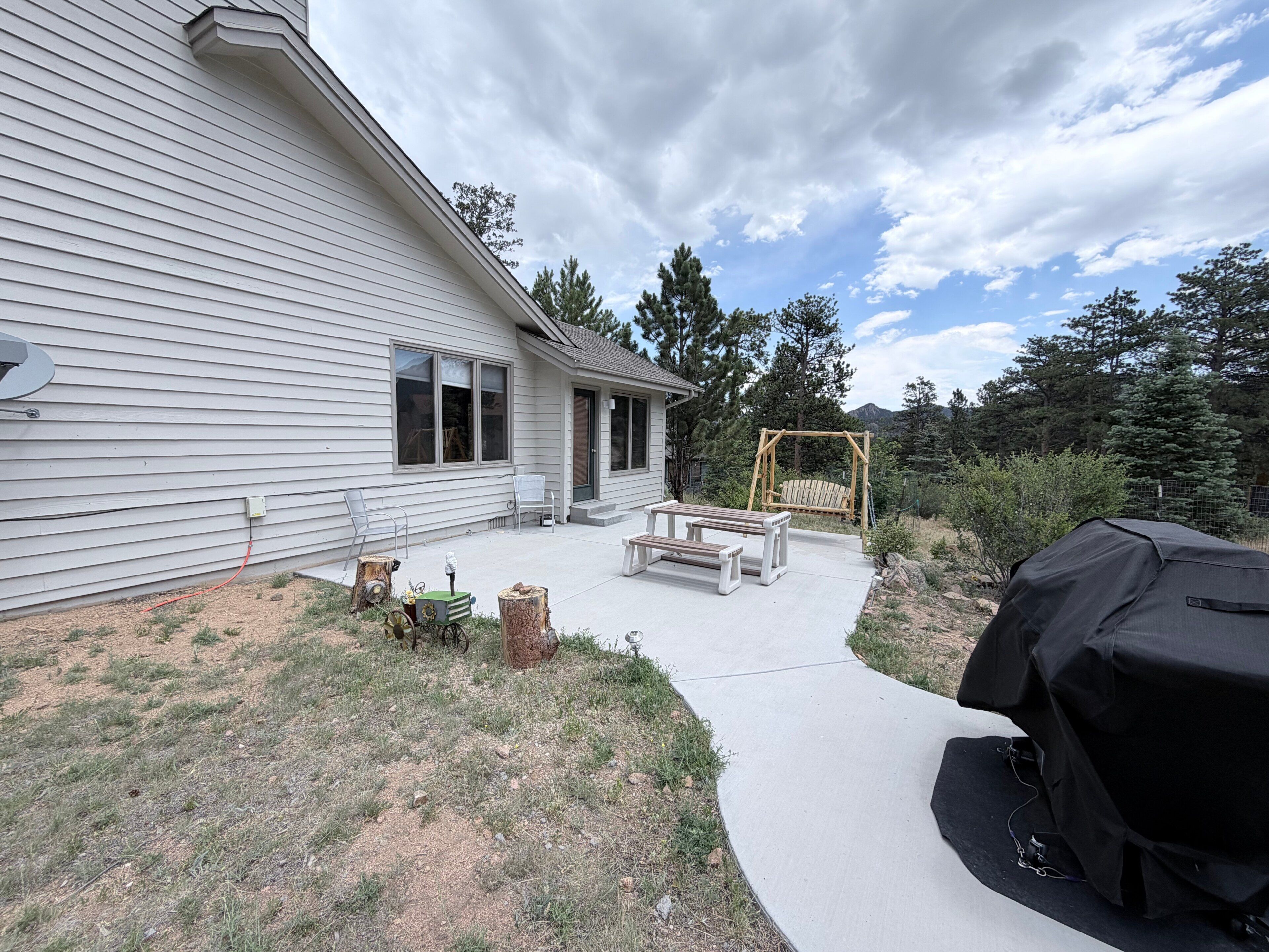 A house with a covered patio, a swing set, and a grill.