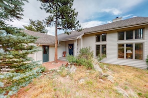 A two-story house with a front porch, a door with a wreath, and a small garden with a tree and shrubs. - Spacious, Dog-friendly Home w/ Private Hot Tub on Large Deck, Mtn Views (Estes Park)