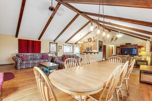 A spacious living area with a large wooden dining table, multiple chairs, a sofa, and a kitchen in the background. - Three BR With Epic Mountain Views and Huge Deck! (Estes Park)