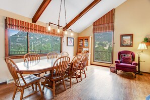 A dining area with a wooden table and chairs, large windows with a view, and a red armchair. - Three BR With Epic Mountain Views and Huge Deck! (Estes Park)