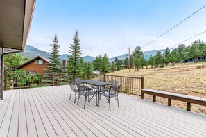 A wooden deck with a table and chairs, overlooking a mountainous landscape with trees and a house. - Three BR With Epic Mountain Views and Huge Deck! (Estes Park)