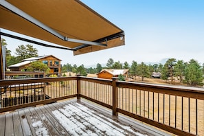 Eine Holzterrasse mit Metallgeländer, einem ausrollbaren Sonnensegel und Blick auf eine Wohngegend mit Häusern und Bäumen.