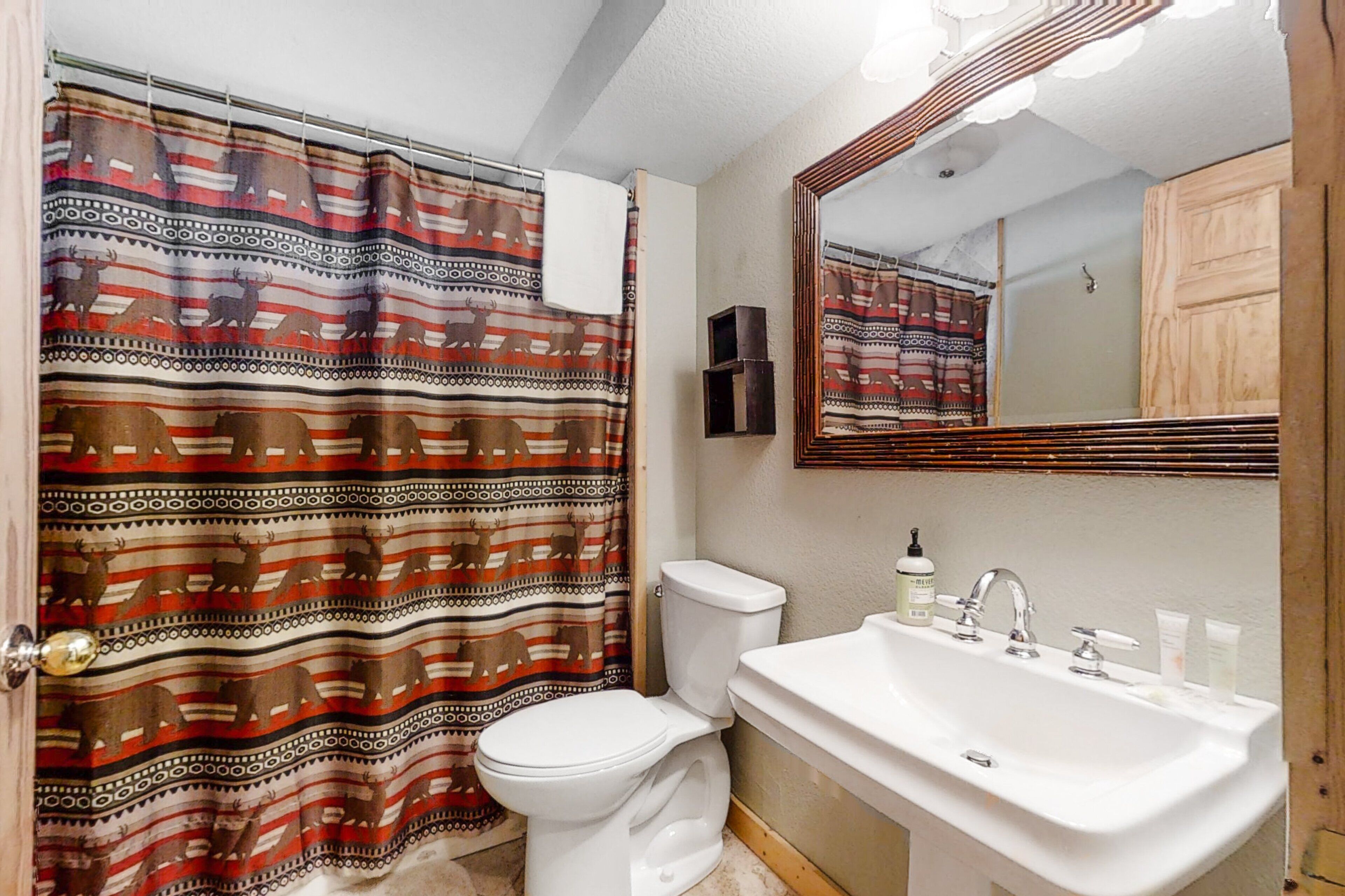 A bathroom with a patterned shower curtain, a toilet, a sink with toiletries, and a mirror.