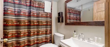 A bathroom with a patterned shower curtain, a toilet, a sink with toiletries, and a mirror.