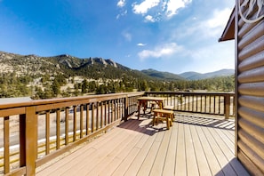 Eine Holzdielen-Terrasse mit Tisch und Stühlen, mit Blick auf eine gebirgige Landschaft.