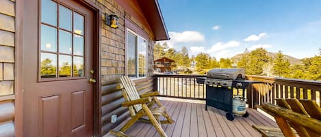 A wooden deck with a grill, rocking chairs, and a door.