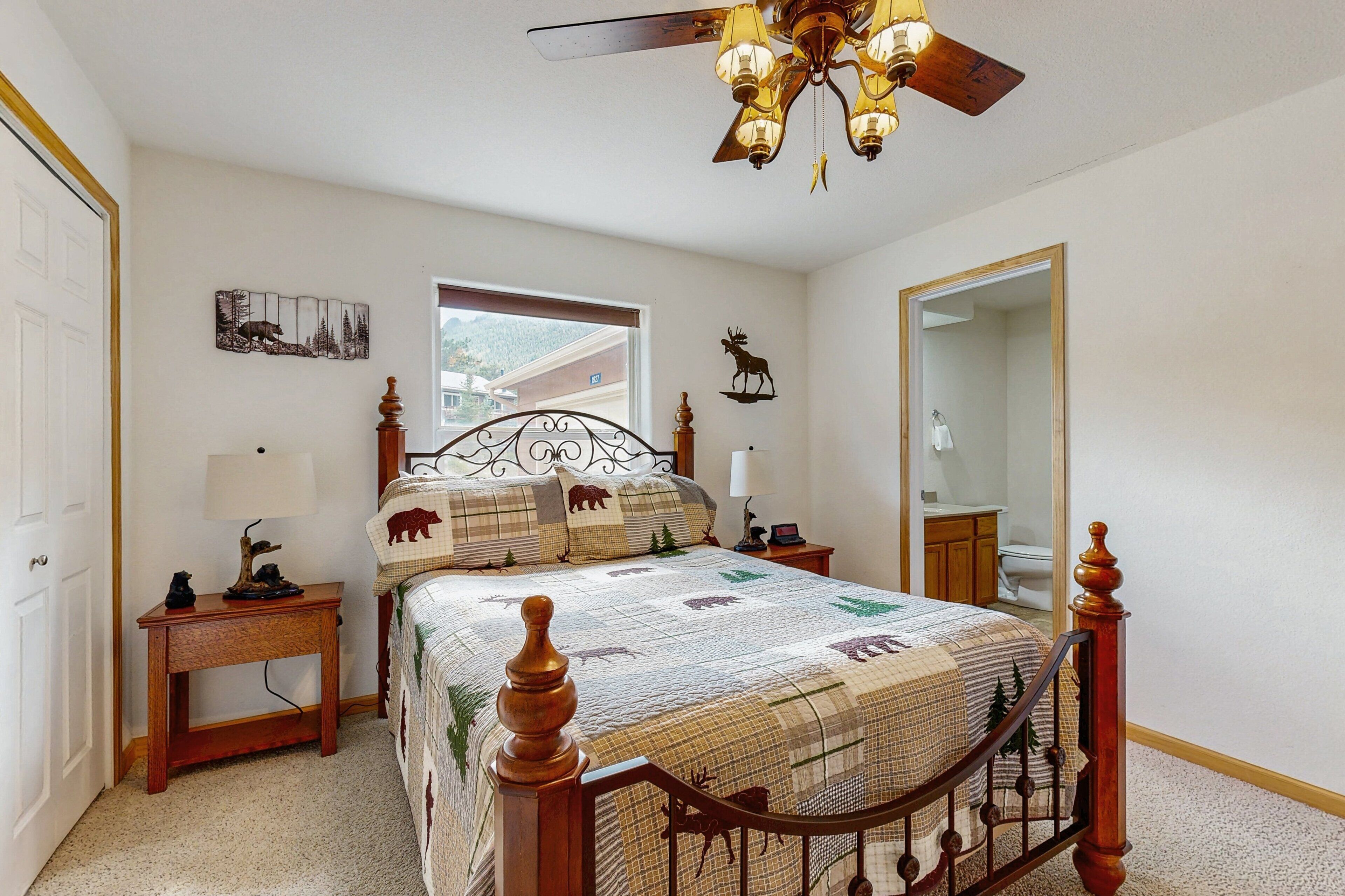 A bedroom with a bed, a bedside table, a nightstand, a ceiling fan, a window, and a mirror.