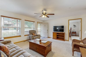 A spacious living room with a ceiling fan, a large flat-screen TV, a wooden coffee table, and a comfortable sofa. - Conveniently Located Home w/ Full Kitchen, Deck & Mountain Views (Estes Park)