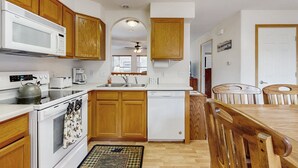 Una cocina con armarios de madera, microondas, horno, lavavajillas y una mesa de comedor con sillas.