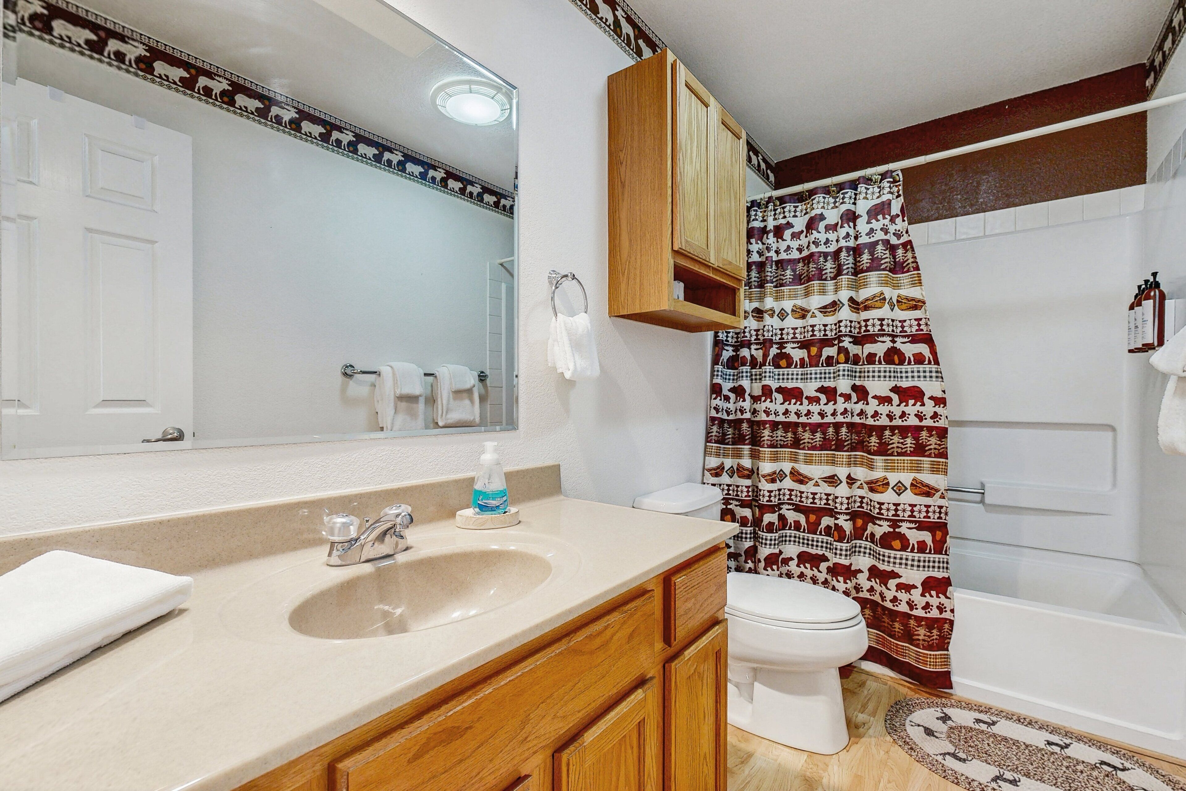 A bathroom with a sink, mirror, wooden cabinets, toilet, and a shower curtain with a pattern.