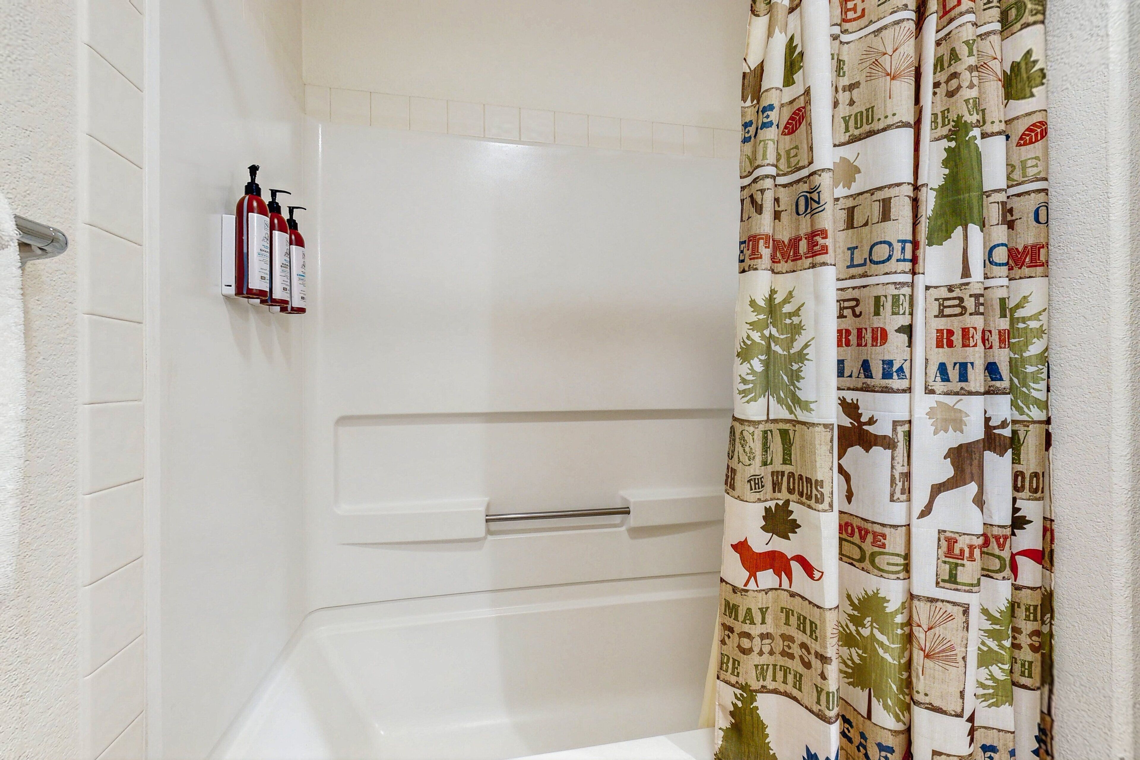 Un baño con una bañera blanca, un perchero con botellas y una cortina de ducha con motivos forestales.