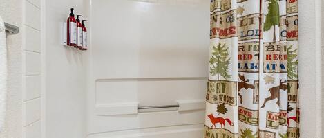Un baño con una bañera blanca, un perchero con botellas y una cortina de ducha con motivos forestales.