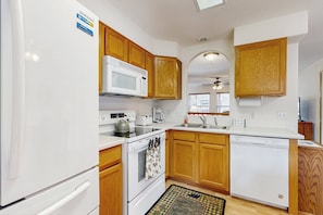 A kitchen with white appliances, wooden cabinets, a microwave, a stove, a dishwasher, and a ceiling fan. - Conveniently Located Home w/ Full Kitchen, Deck & Mountain Views (Estes Park)