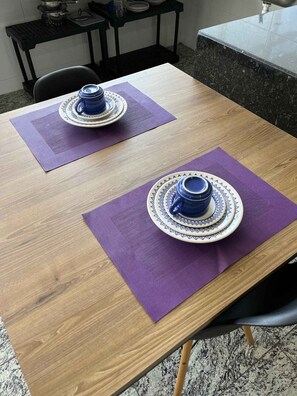 Een houten eettafel met twee blauw-witte theeserviezen op paarse placemats.
