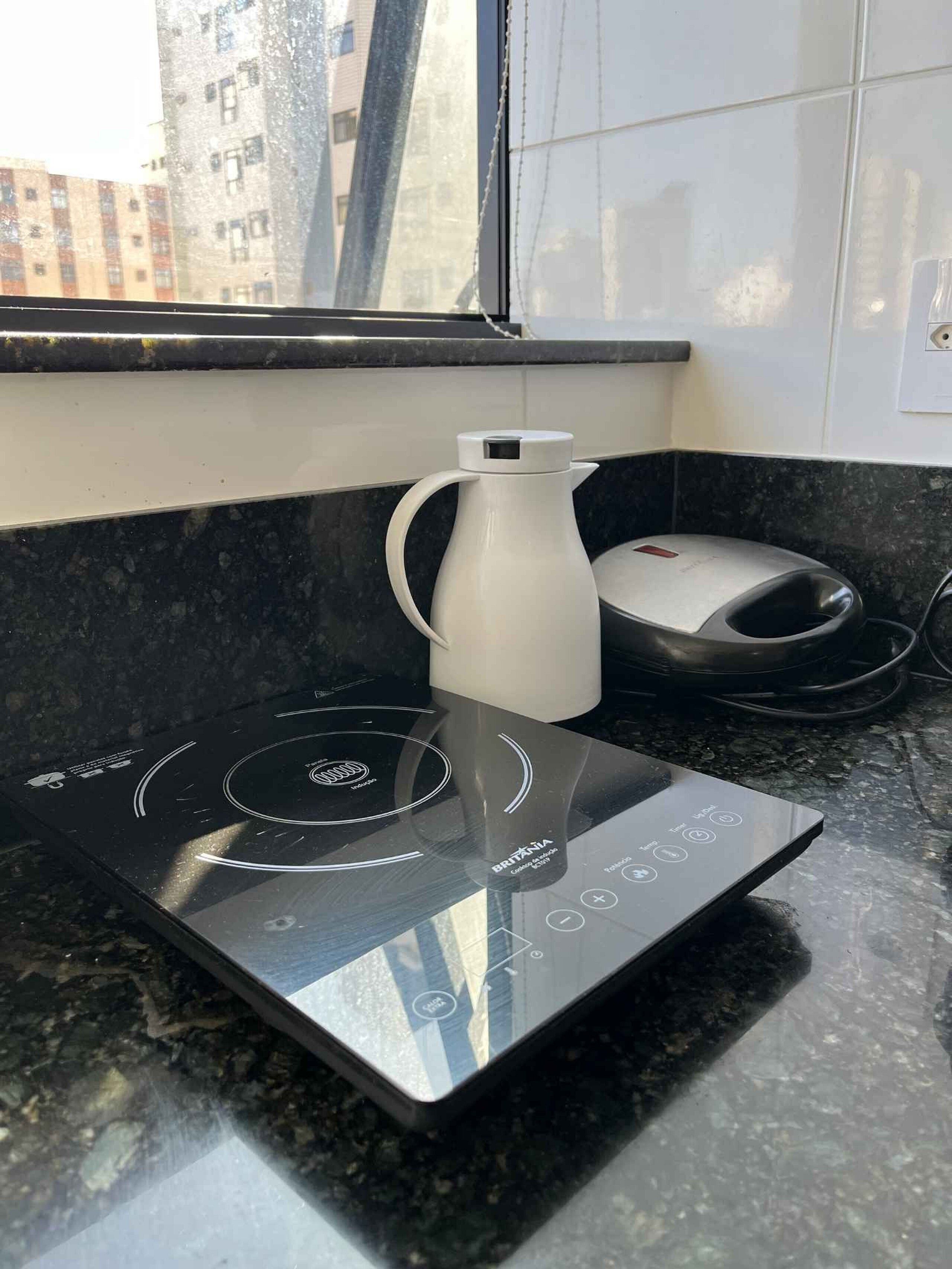 Una cucina con un piano cottura a induzione nero, un bollitore elettrico bianco e una macchina da caffè su un bancone in granito.