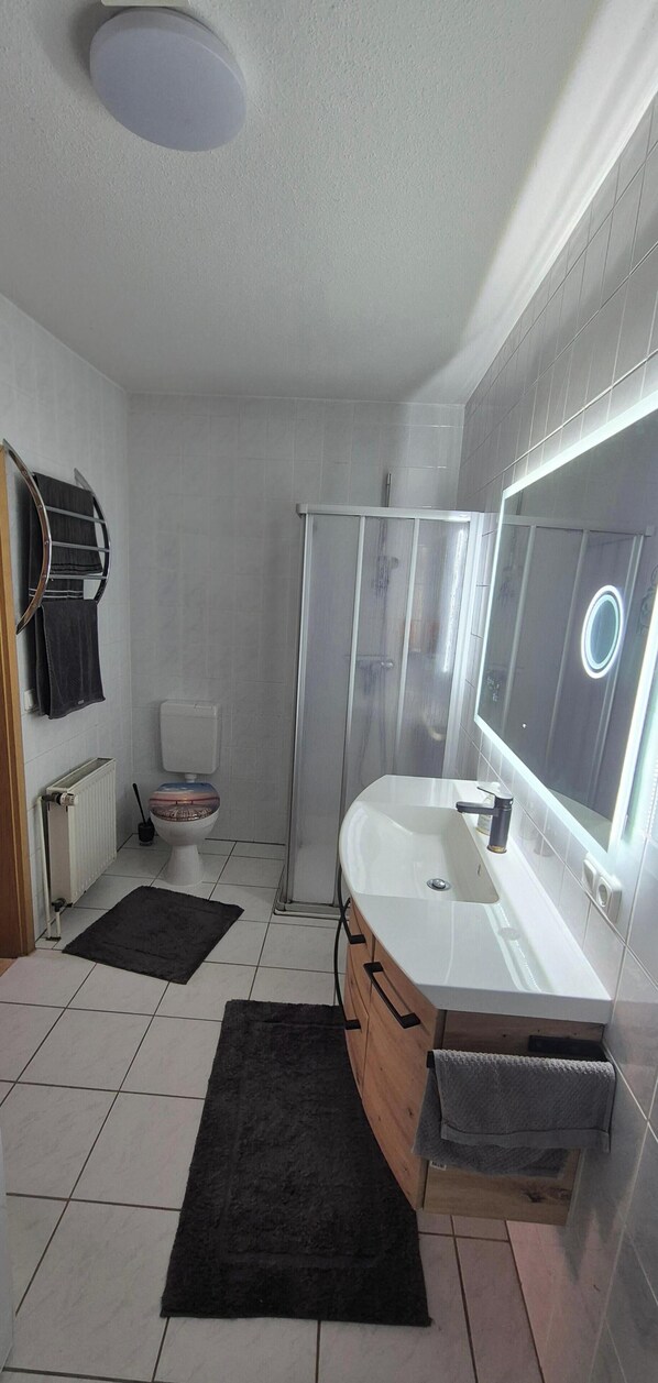 A modern bathroom with a white sink, a mirror, a shower enclosure, and a toilet. - Coach house at the Amber Castle (Kuhlen-Wendorf)