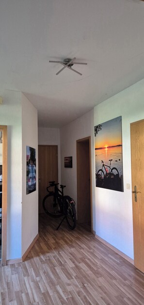A hallway with wooden flooring, a ceiling fan, and two doors. One door has a bicycle leaning against it. - Coach house at the Amber Castle (Kuhlen-Wendorf)