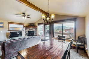 A spacious dining area with a wooden table and chairs, a sofa, a fireplace, and a large window with a view of mountains.