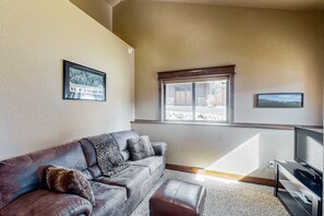 A living room with a leather sofa, a television, and a window with a view of a building.