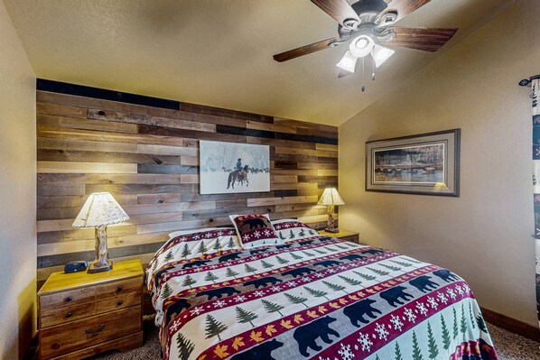 A bedroom with a wooden headboard, a bed with a patterned bedspread, two bedside tables with lamps, and a ceiling fan.
