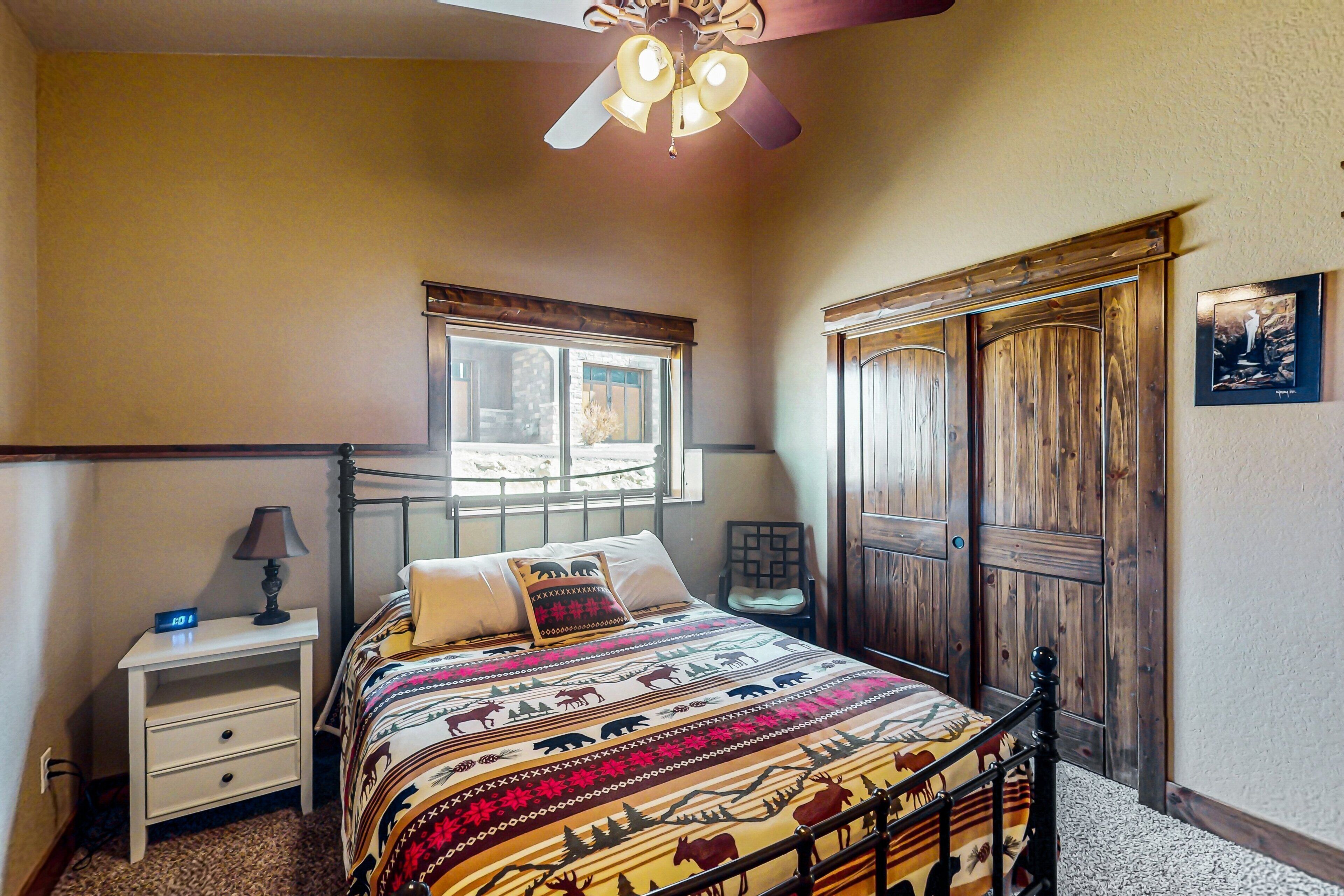 A bedroom with a bed, a nightstand, a chair, a window, a wooden wardrobe, and a ceiling fan.