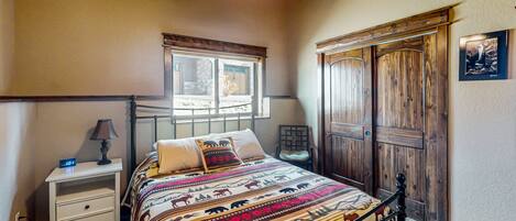 A bedroom with a bed, a nightstand, a chair, a window, a wooden wardrobe, and a ceiling fan.