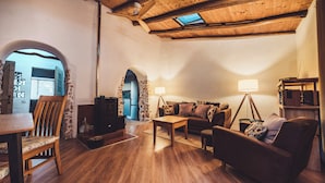 A cozy living room with wooden flooring, a sofa, a coffee table, and a TV. There is a stone archway leading to another room.