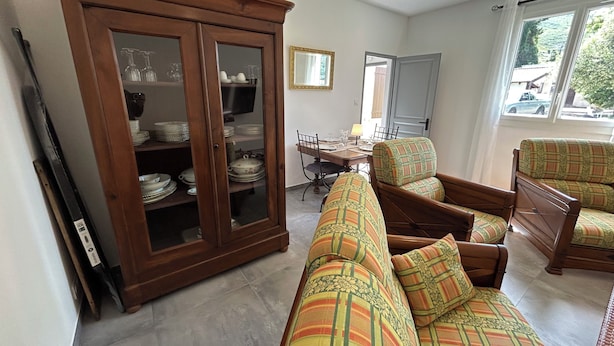 Een woonkamer met een bank, stoelen, een kast met glazen deuren, een eettafel en een televisie.