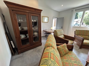 A living room with a sofa, chairs, a cabinet with glass doors, a dining table, and a television.