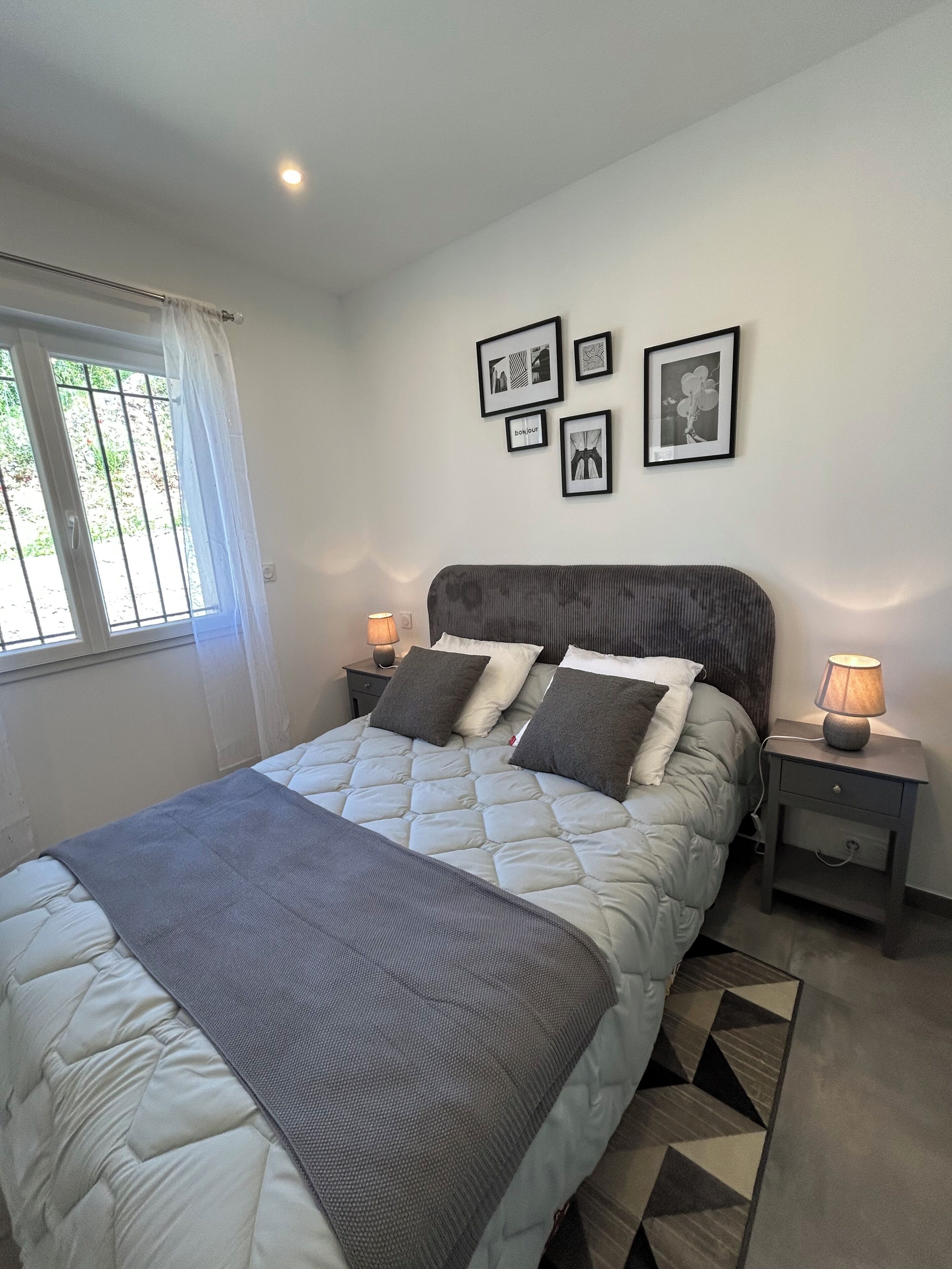 Ein Schlafzimmer mit einem Bett, zwei Nachttischen, einem Fenster mit Vorhängen und Wandbildern.