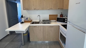 Een compacte keuken met houten kastjes, een wit aanrecht, een spoelbak, een magnetron en een koelkast.