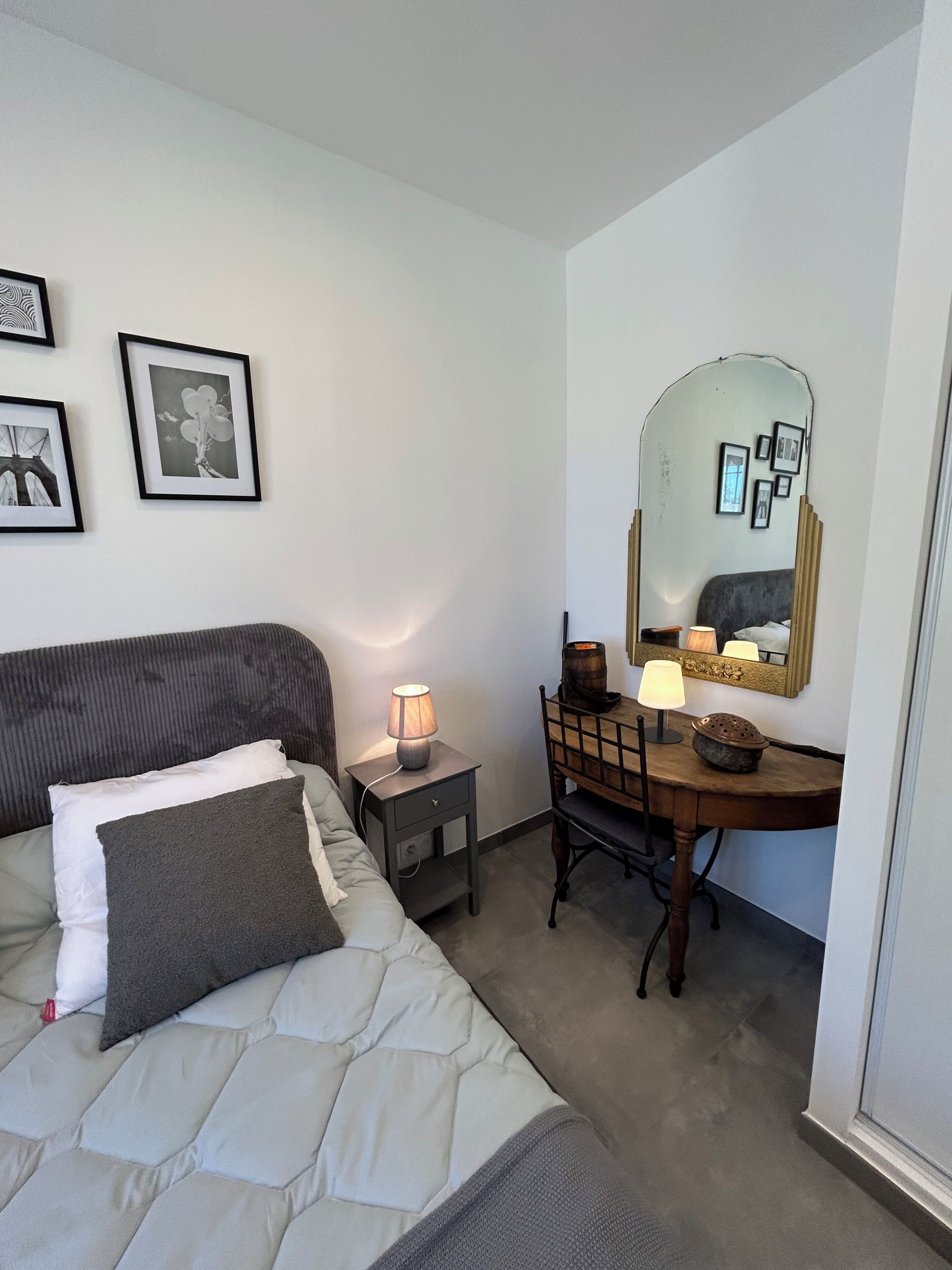 Een slaapkamer met een bed, nachtkastje, lamp, kapstok, spiegel en ingelijste foto's aan de muur.