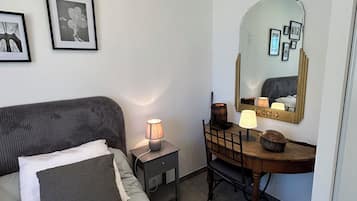Een slaapkamer met een bed, nachtkastje, lamp, kapstok, spiegel en ingelijste foto's aan de muur.